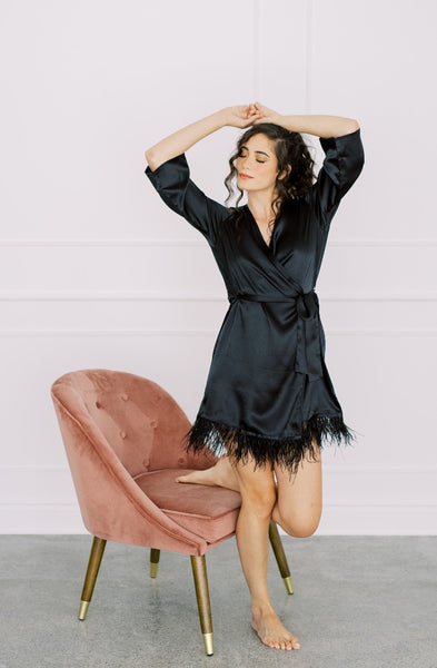 a model lounging in by catalfo's black satin feather trim robe
