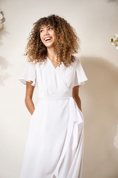 a model shows off pockets on a simple and elegant, white wedding wrap dress