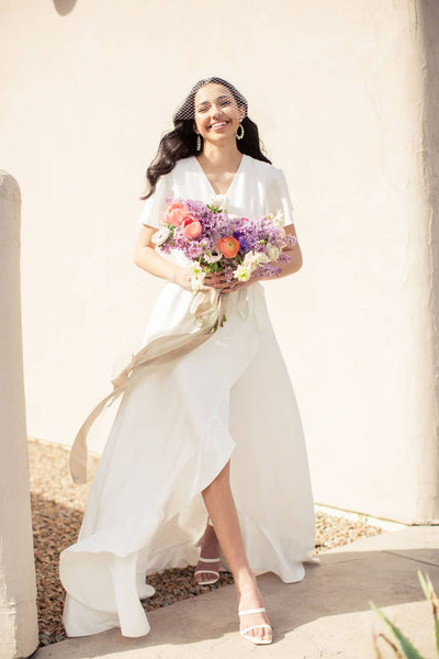 a bride holds a bouquet wearing modern and simple wedding dress with ruffle hemline