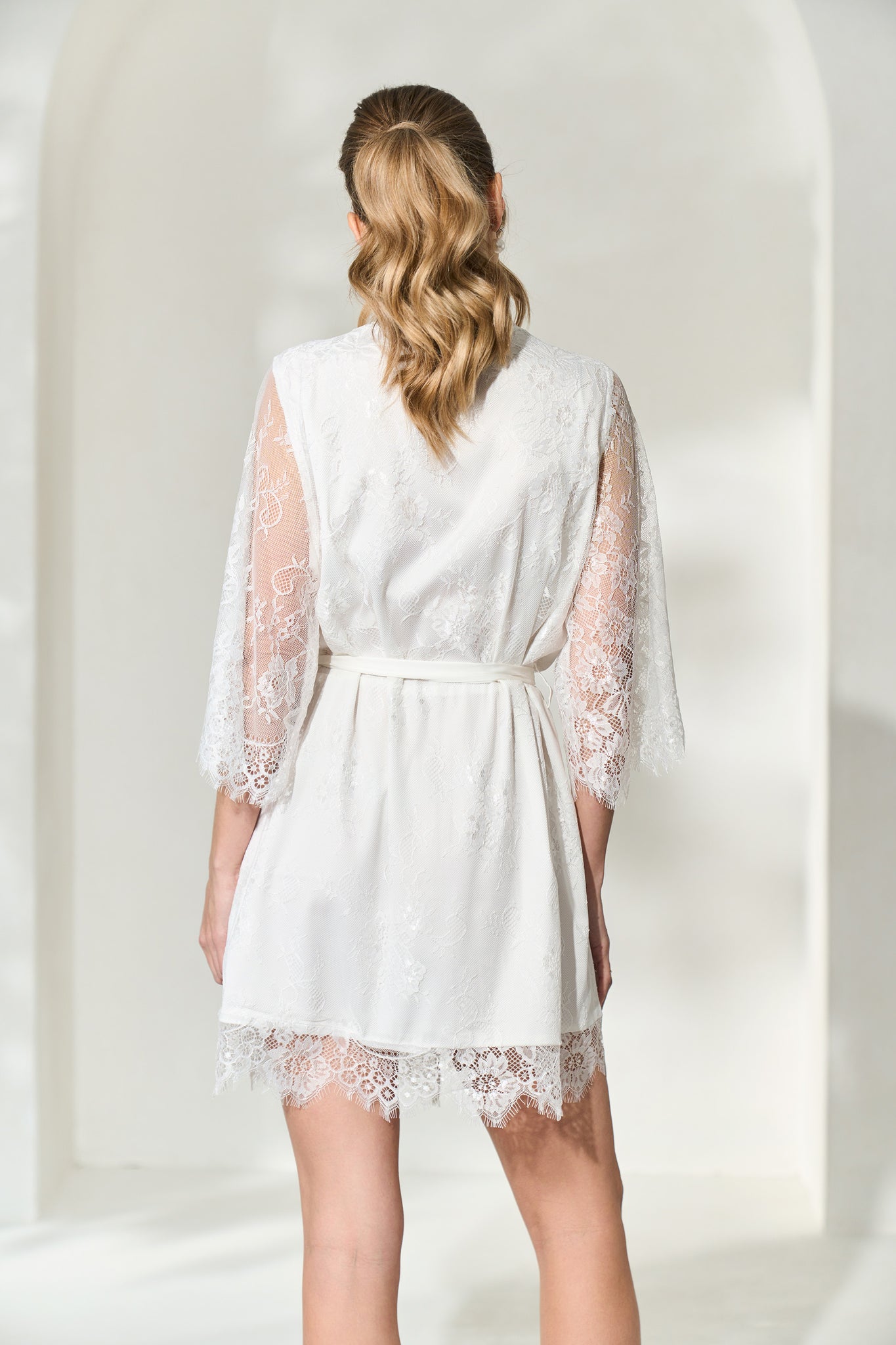 Back view of woman wearing white lace bridal robe will full length lace sleeves. 