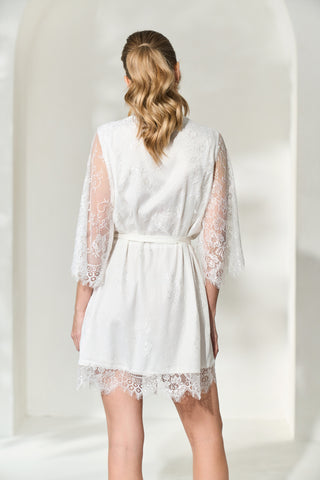 Back view of woman wearing white lace bridal robe will full length lace sleeves. 