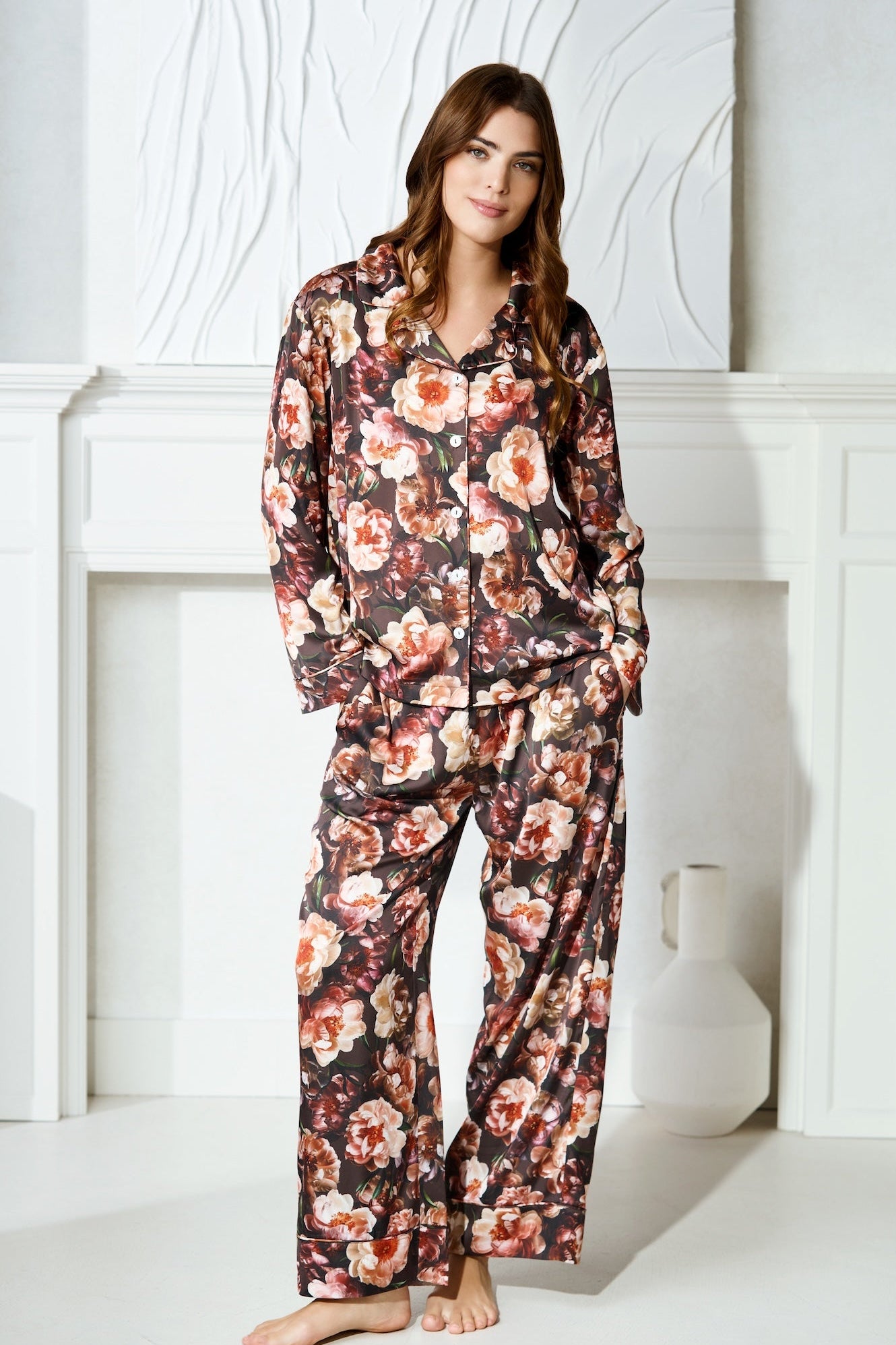 A women wearing a long sleeve pyjama top and pants with her hands in pockets. The pj set is made in a floral print, silky and luxurious material.
