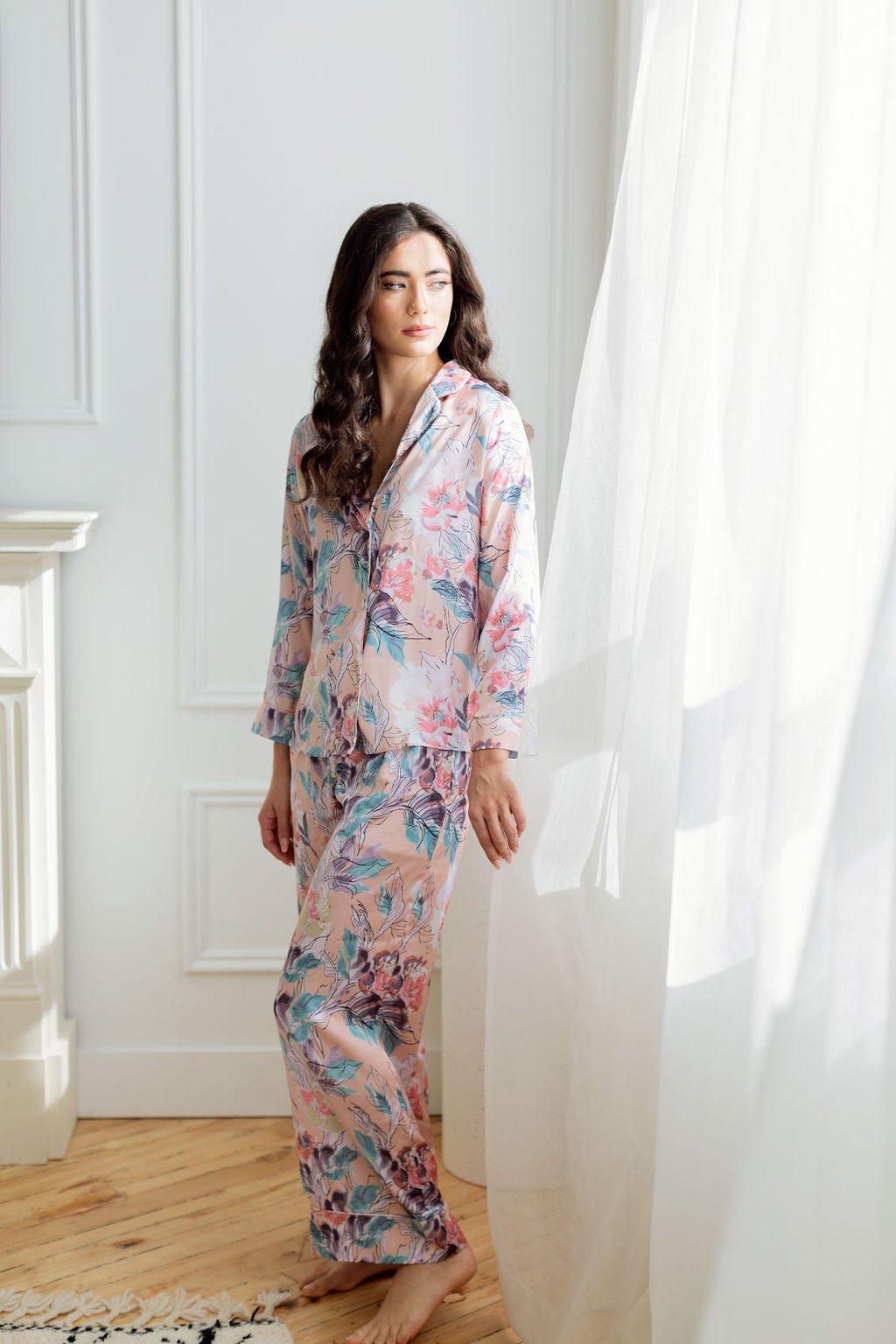 Woman standing beside billowing curtain wearing pink floral print pajama set