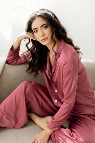 Woman sitting on couch wearing long sleeve red pajamas resting her head on her hand.