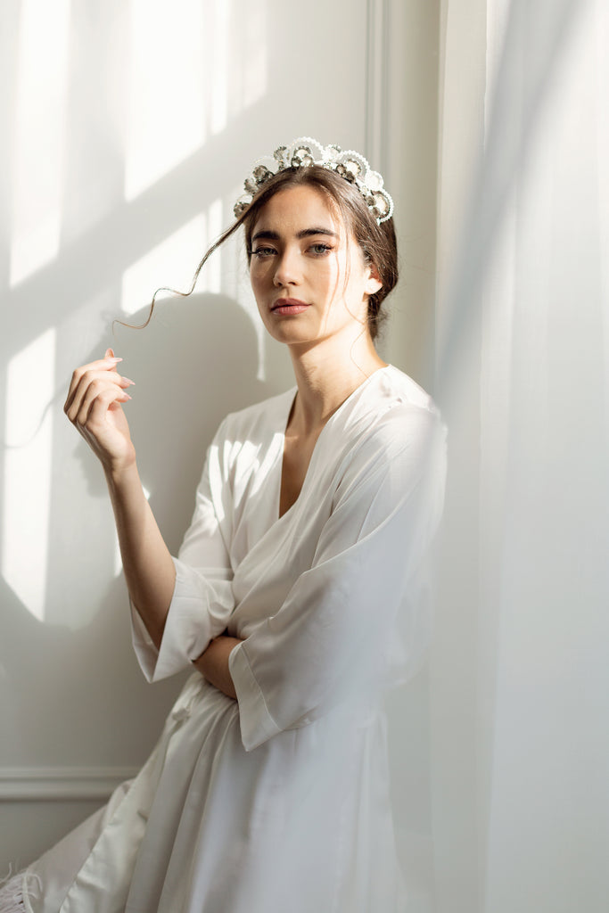 Woman wearing solid white bridal robe while standing beside billowing curtain