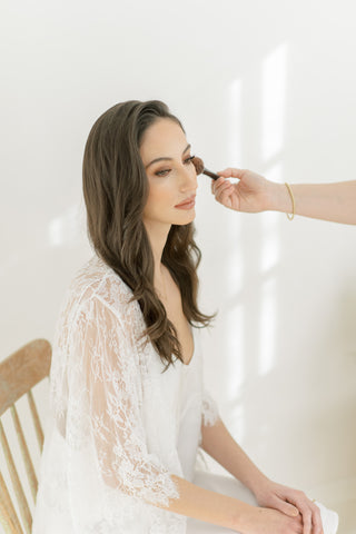 A bride getting her make up done while wearing a long ivory lace robe