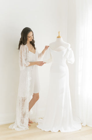 Woman wearing a long lace bridal robe looking at her wedding dress. 