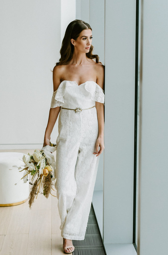 Woman wearing white bridal jumpsuit while looking out a window