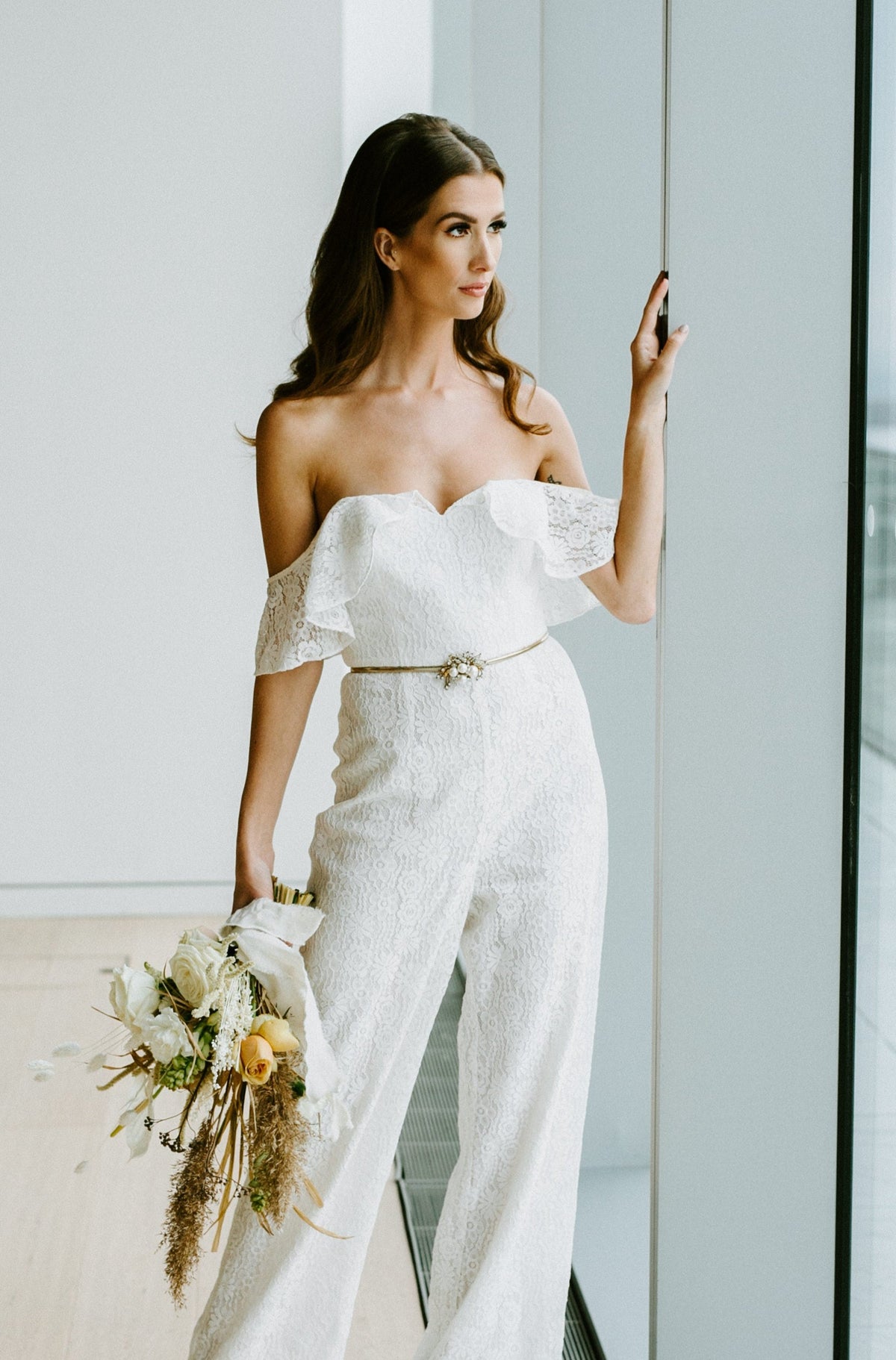 Woman looking out a window wearing a white bridal jumpsuit