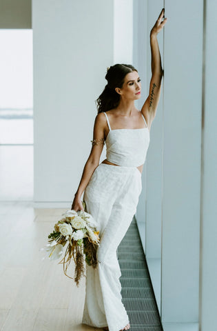 Woman wearing a white bridal jumpsuit leaning against a window