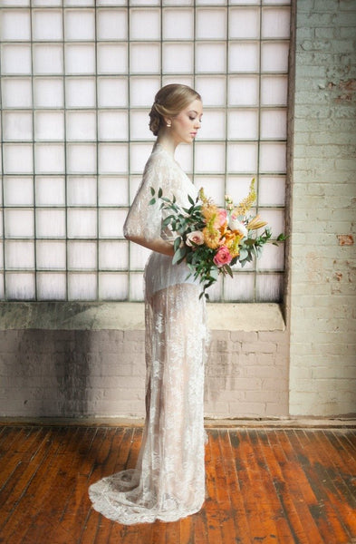 A bride on her wedding day wearing a floor length lace bridal robe and holding a bouquet of flowers