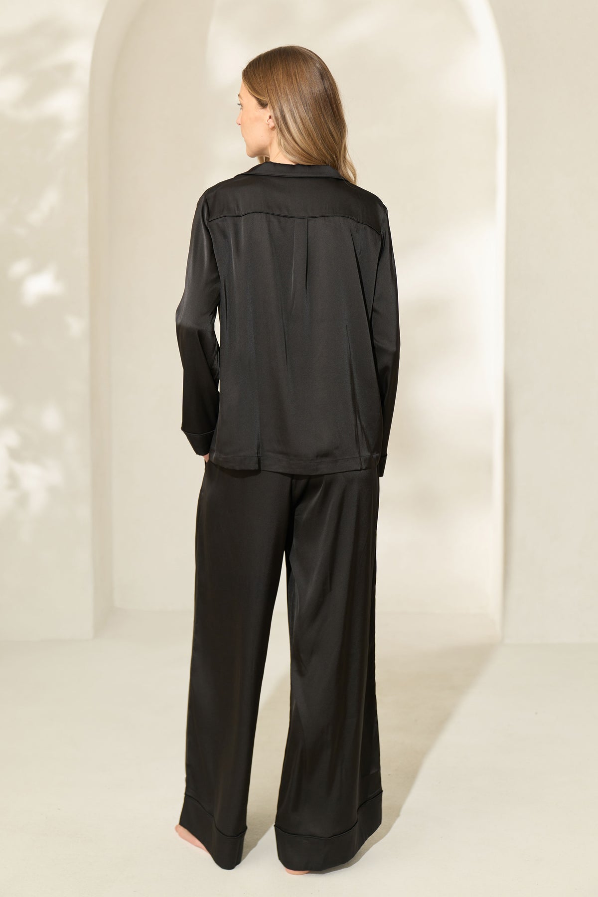 Back view of woman wearing black silky pajamas with sleeve top and elastic drawstring waist band.