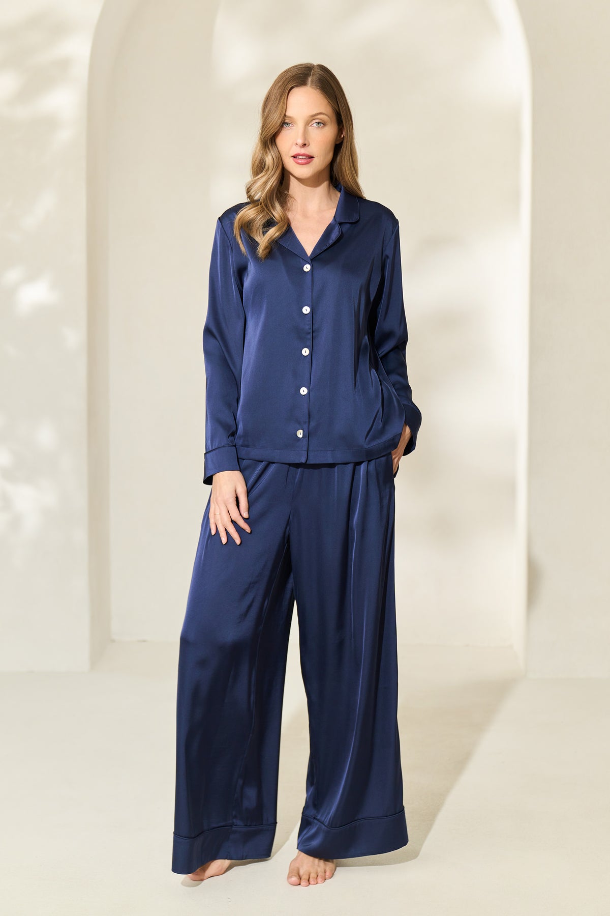 Woman wearing navy silky pajama set with button-up long sleeve top and elastic drawstring waistband