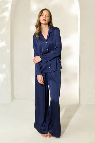 Woman posing while wearing navy silky pajamas with button-up long sleeve top and elastic drawstring waistband