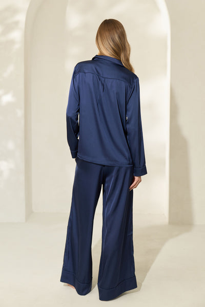 Back view of woman wearing silky navy pajamas with long sleeves and wide pant legs.