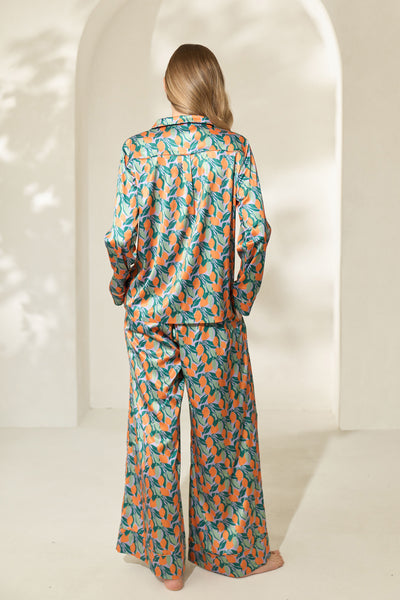 Back view of woman wearing silky pajamas with green and orange citrus fruit print.