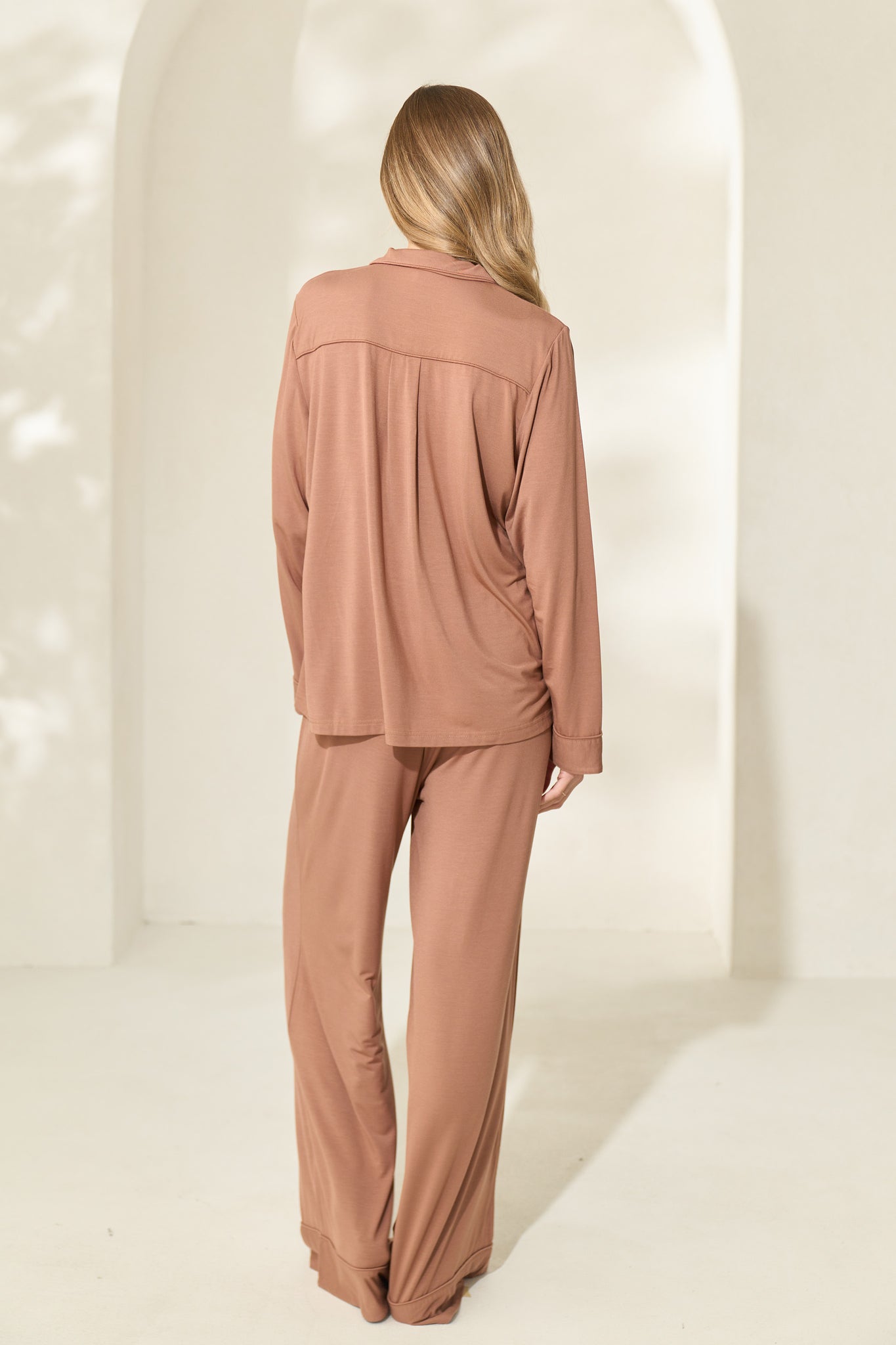 Back view of woman wearing brown modal pajamas with long sleeves and elastic waistband
