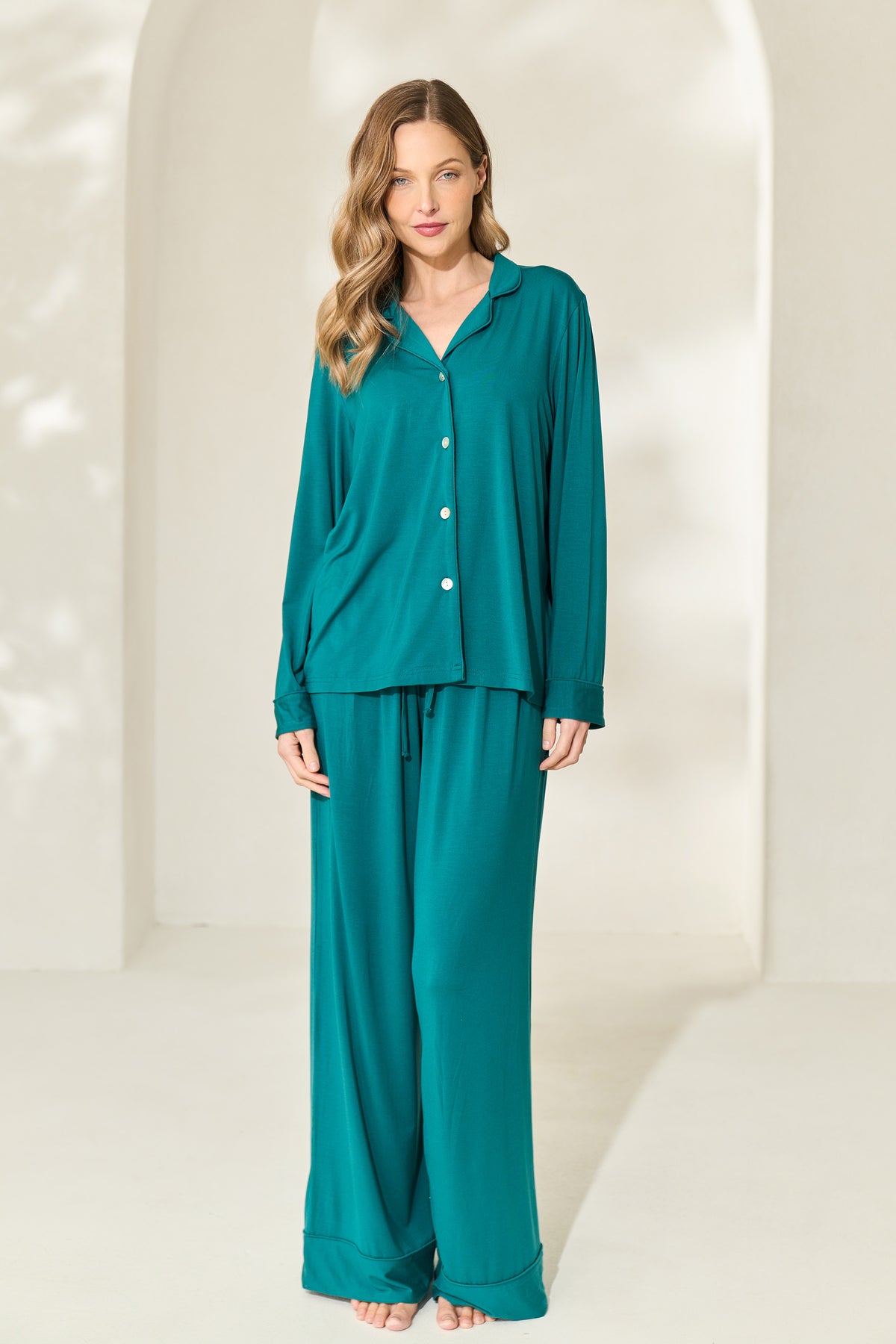 Woman wearing button-up juniper green modal pajamas with long sleeves, elastic waistband and mother of pearl buttons