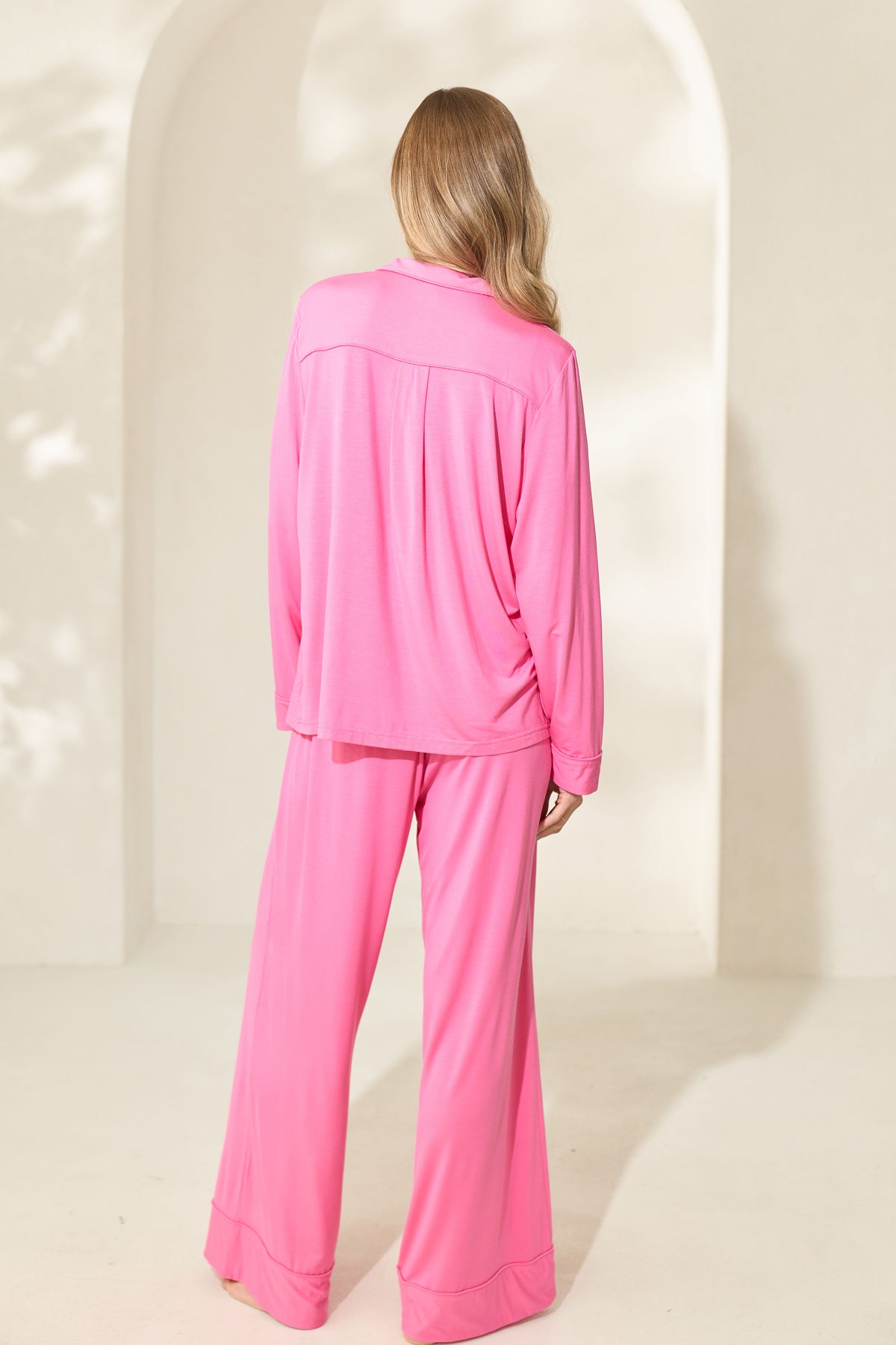 Back view of woman wearing sorbet pink modal pajamas with long sleeves and wide pant legs