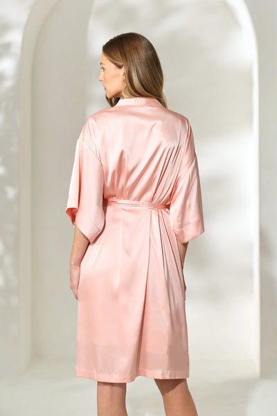 Back view of woman wearing silky knee-length blush pink robe with waist tie.