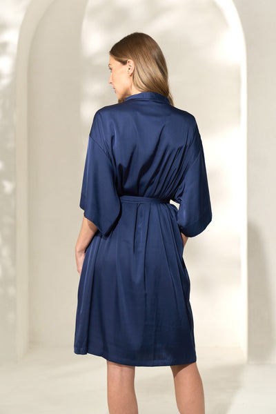 Back view of woman wearing navy silk-like robe with waist tie.