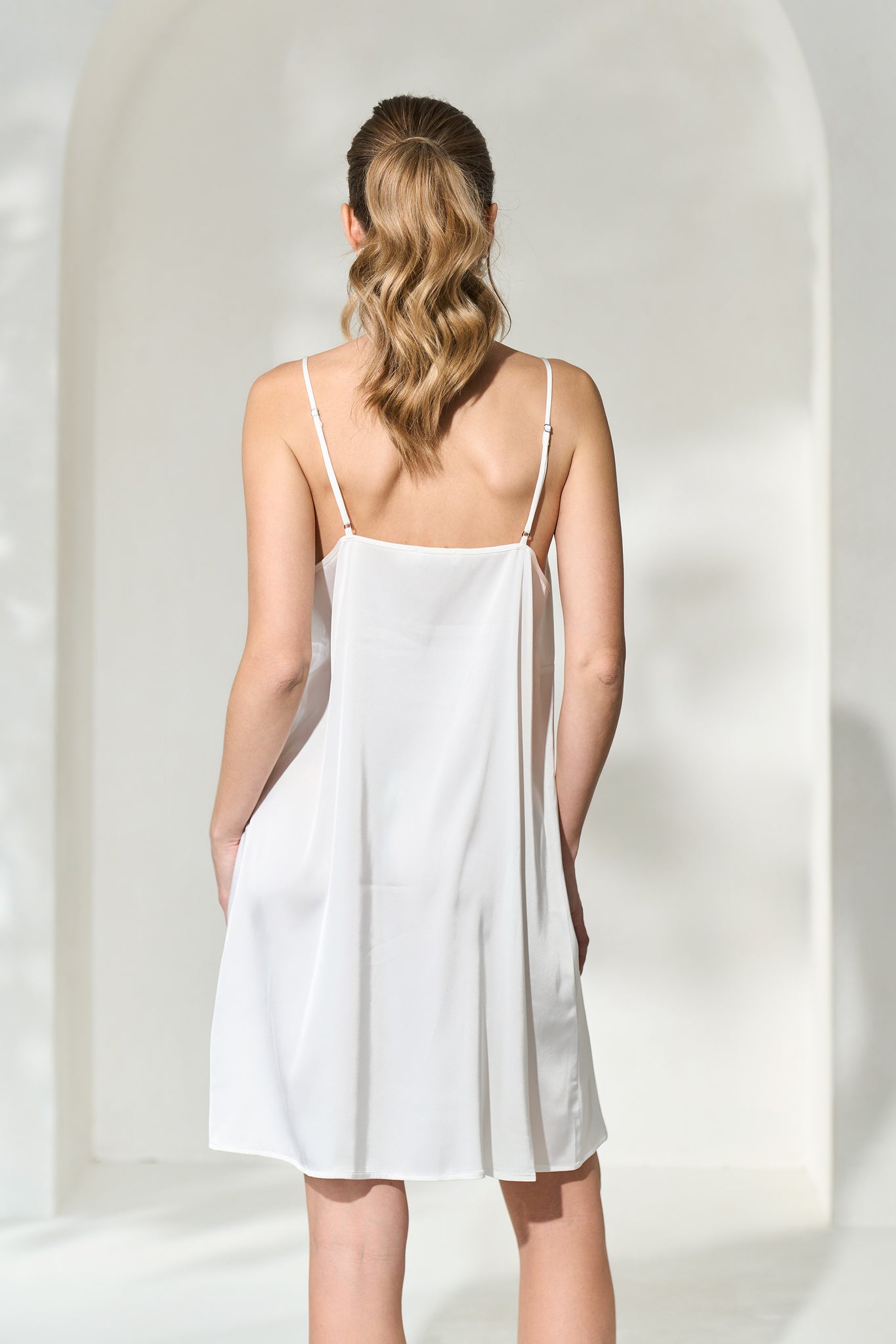 Back view of woman wearing a silk-like white slip dress with adjustable shoulder straps