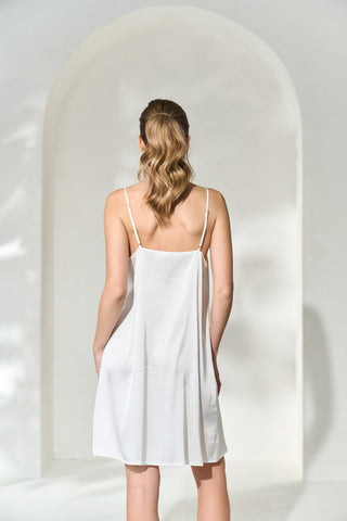 Back view of woman wearing a silk-like white slip dress with adjustable shoulder straps