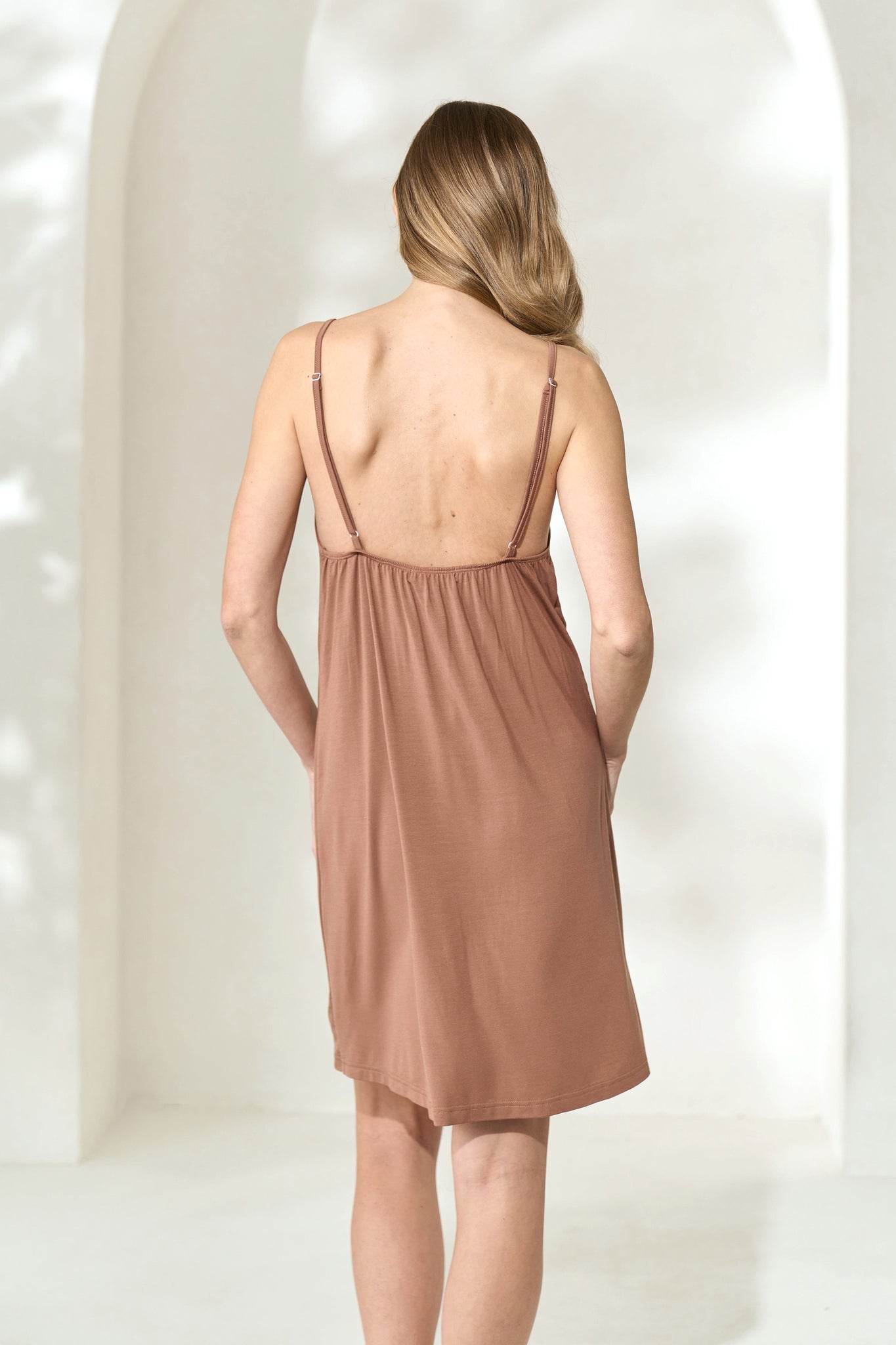 Back view of woman wearing light brown modal slip dress with adjustable shoulder straps