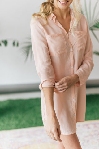 Woman rolling up sleeve of peach colored boyfriend shirt