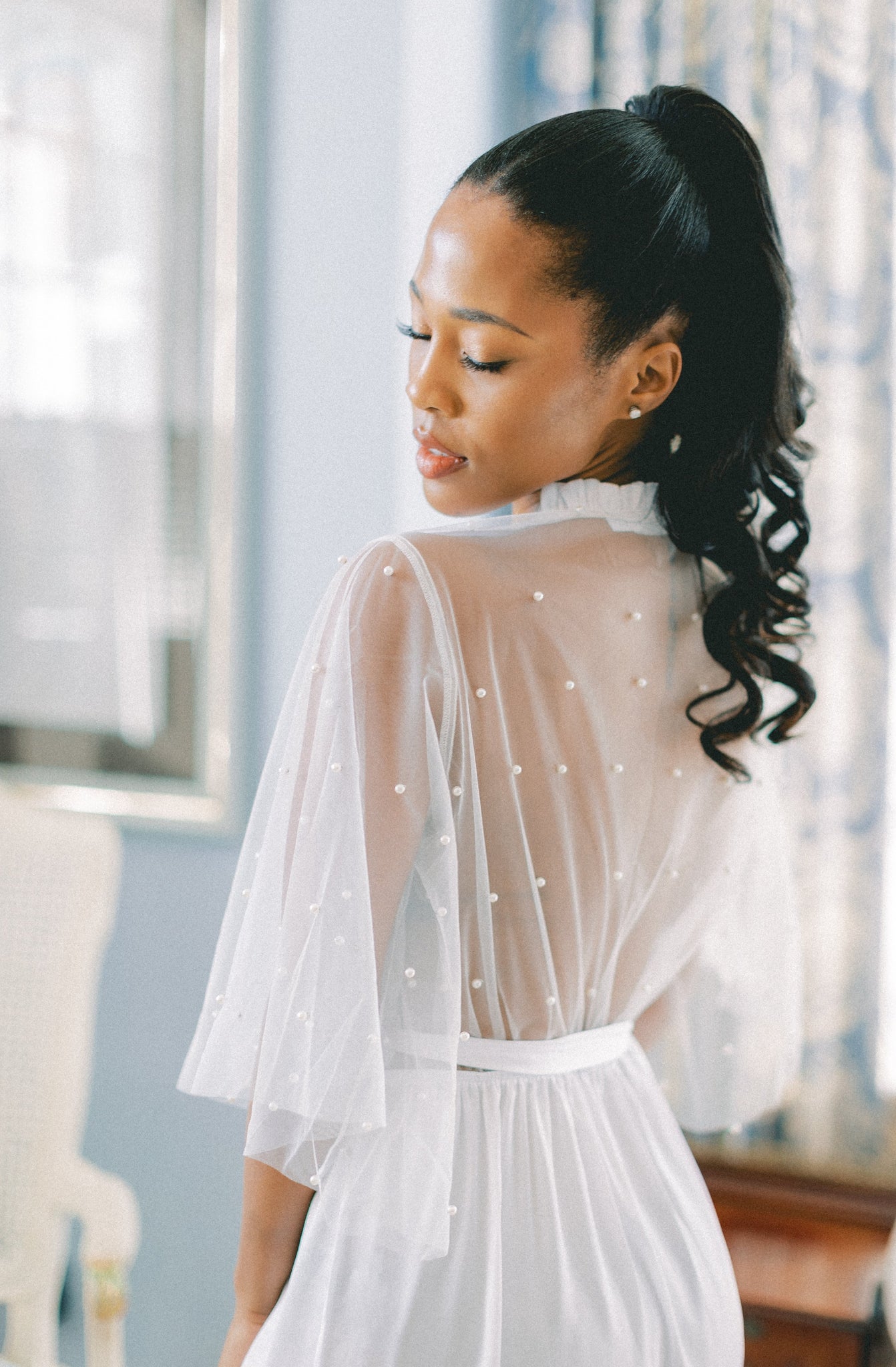 Back view of woman wearing a white bridal robe with pearls on the lace back