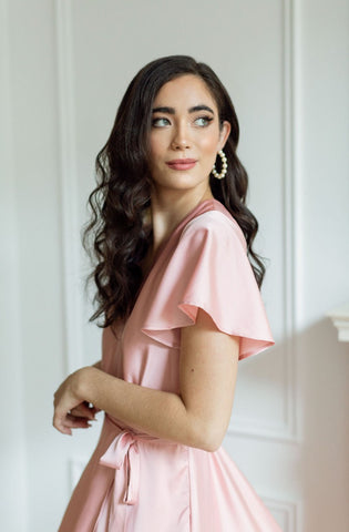 a model styled in pink satin wrap dress with pearl hoop earrings