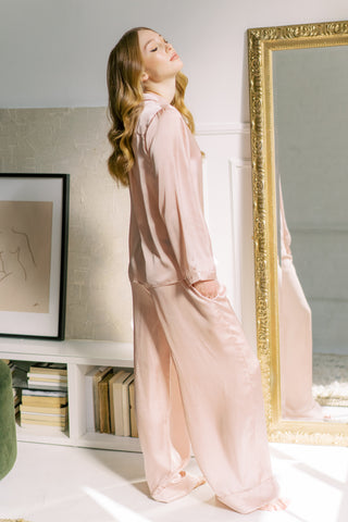 a women posing at home wearing full length, luxury blush pajama set