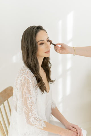 a bride getting make up done wearing by catalfo white lace bridal robe