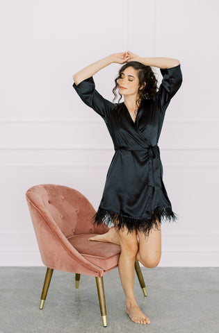 a model lounging in by catalfo's black satin feather trim robe